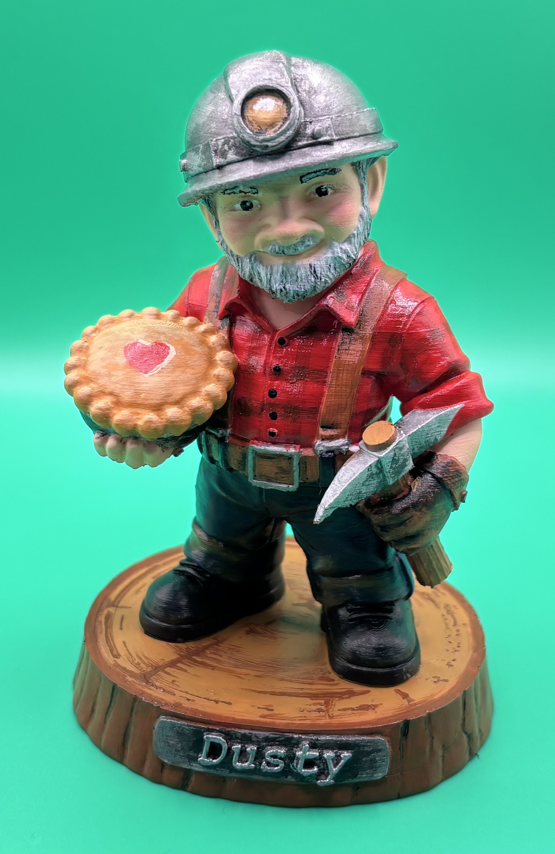 Custom 3D printed miner figurine named Dusty, holding a pie and pickaxe, created as a personalized retirement keepsake.