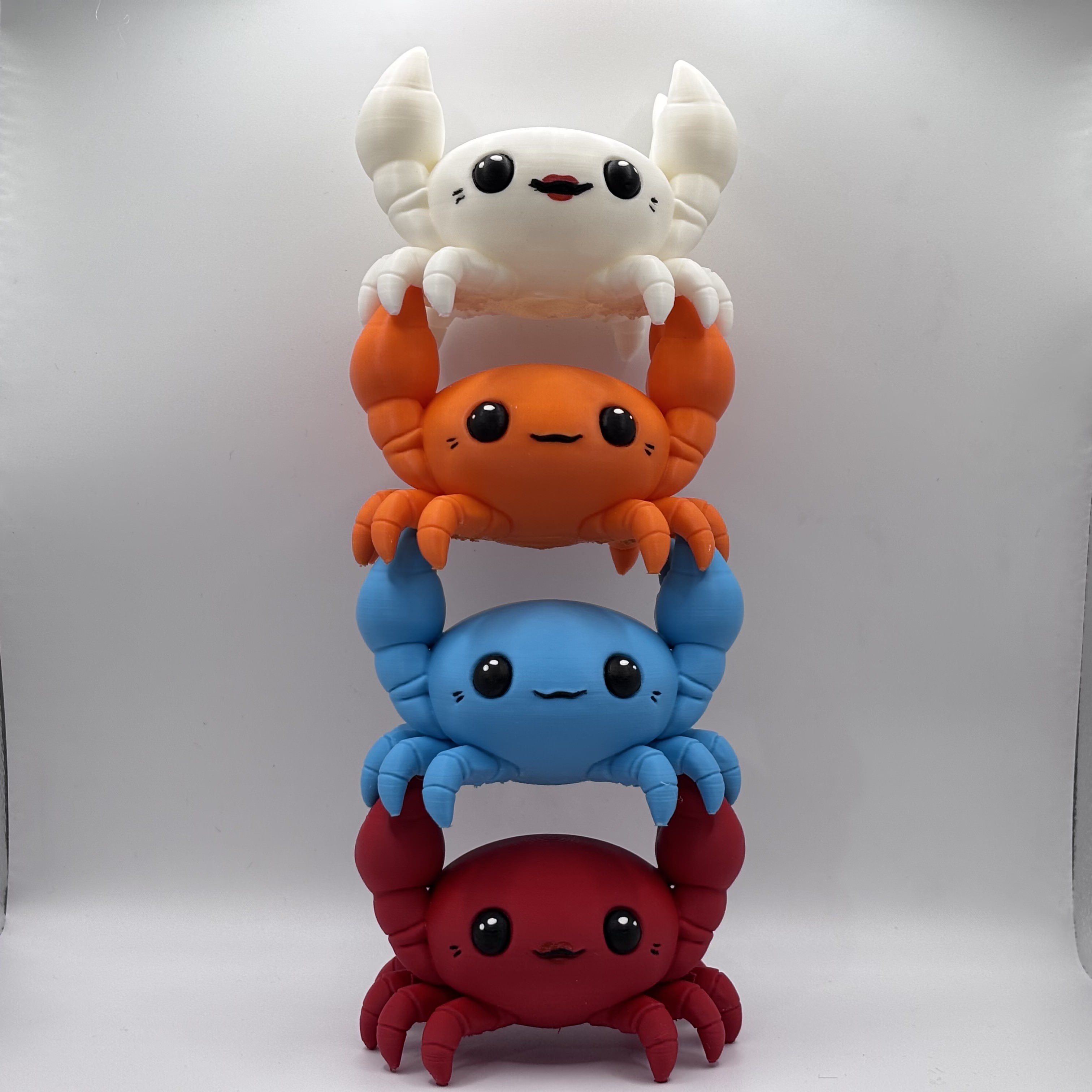 Stacked chibi-style crab figurines in white, orange, blue, and red, 3D printed and designed as cute desk décor collectibles.