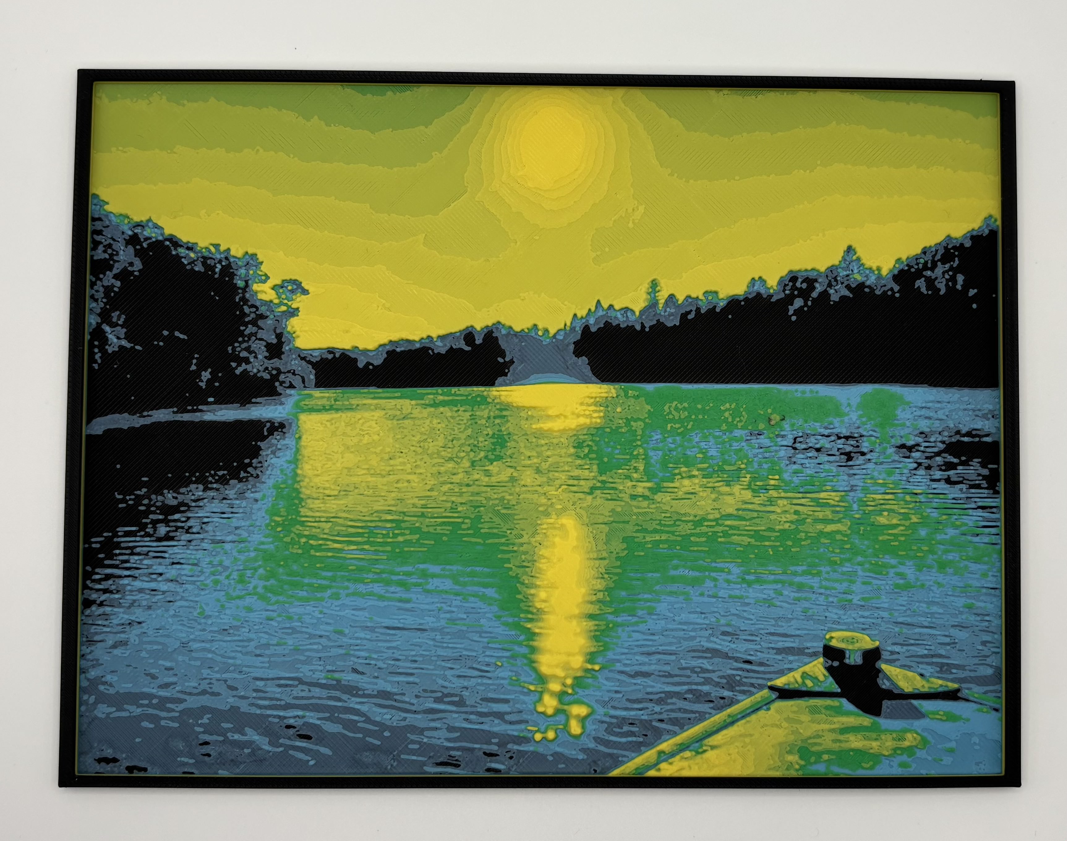 HueForge 3D printed wall art showing a yellow sunset over a calm lake with green 		reflections and dark tree silhouettes, framed minimalist landscape print