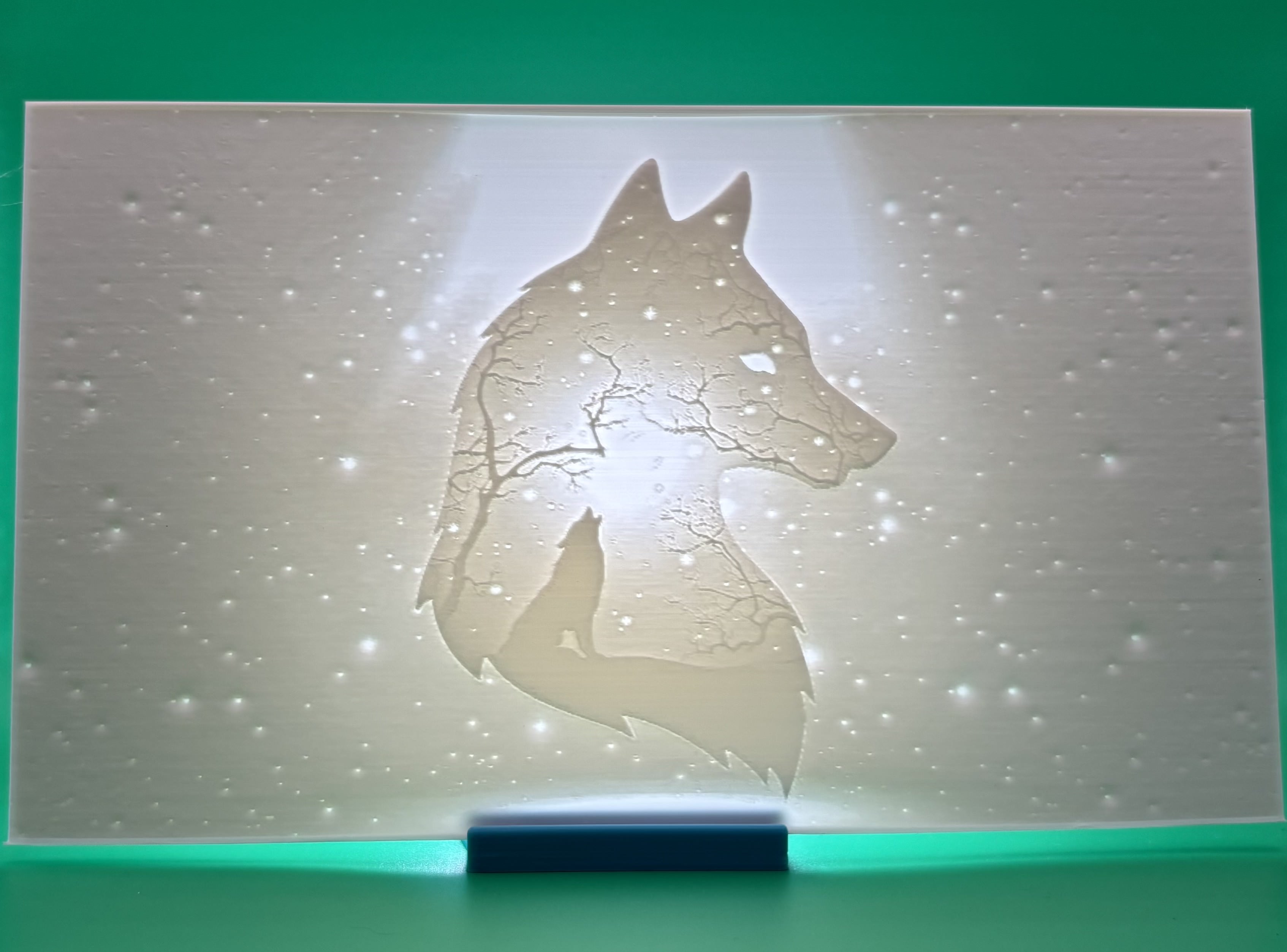 Custom 3D printed lithophane of a wolf silhouette filled with trees and a starry 		night sky, backlit nature-inspired wall art