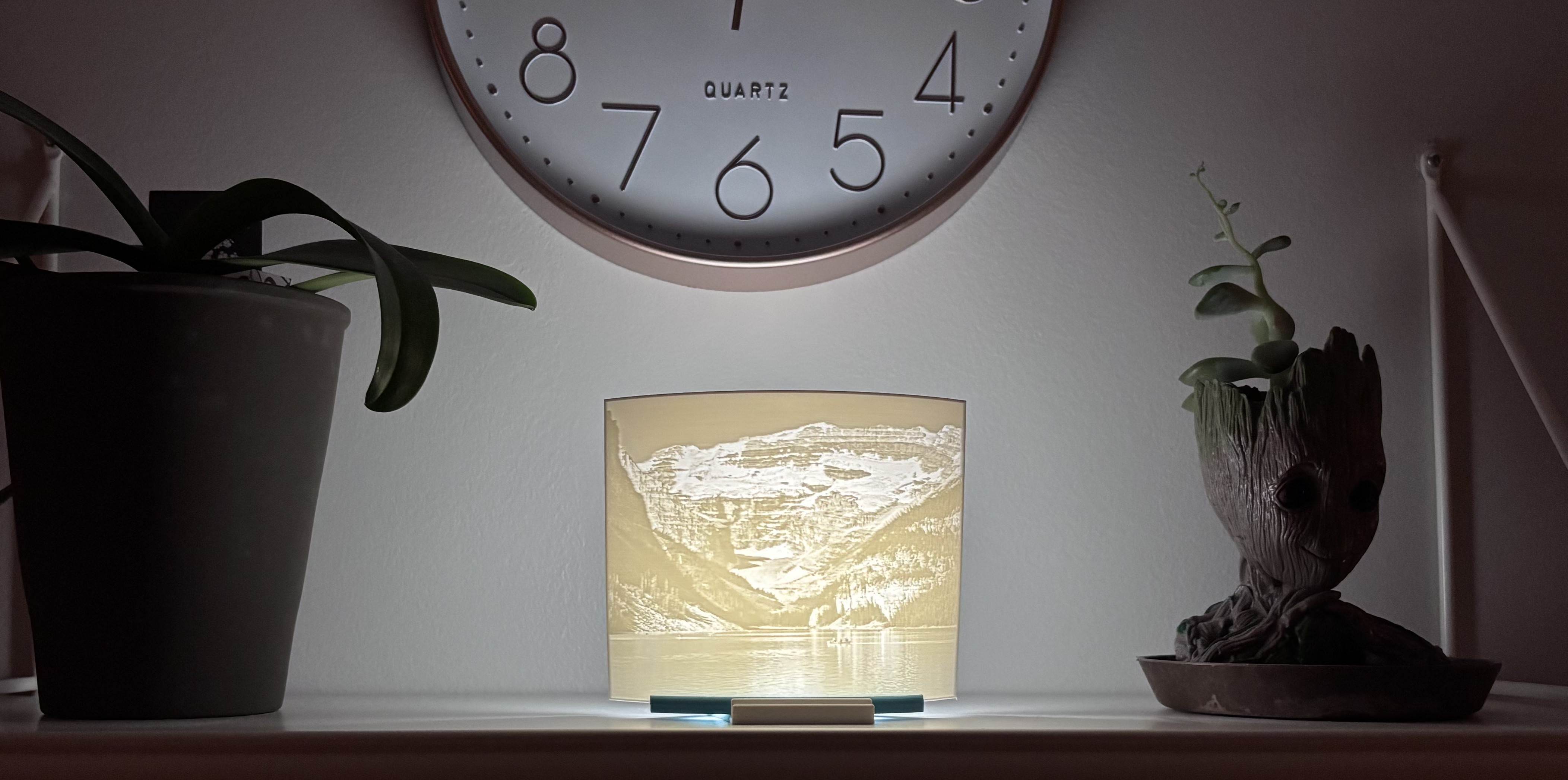 3D printed landscape lithophane showing a mountain lake scene with cliffs and water reflection illuminated on a light base